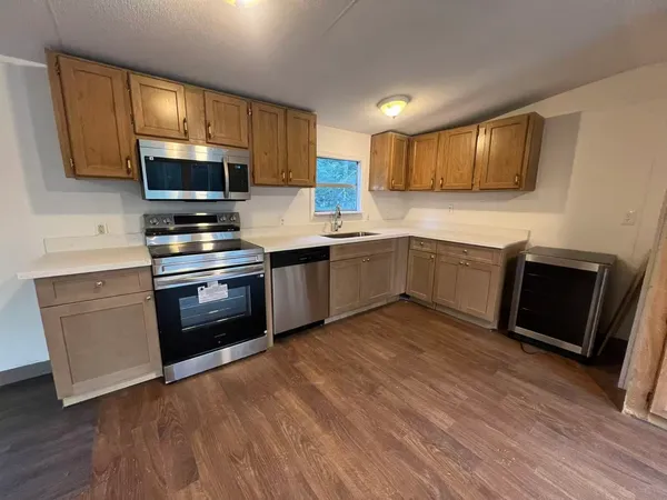 a kitchen with stainless steel appliances granite countertop a stove top oven a sink dishwasher and a microwave oven on the wooden floors