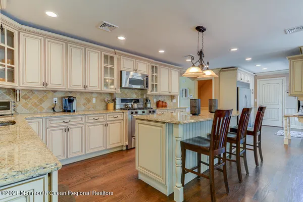 a kitchen with kitchen island granite countertop wooden floors white cabinets and stainless steel appliances