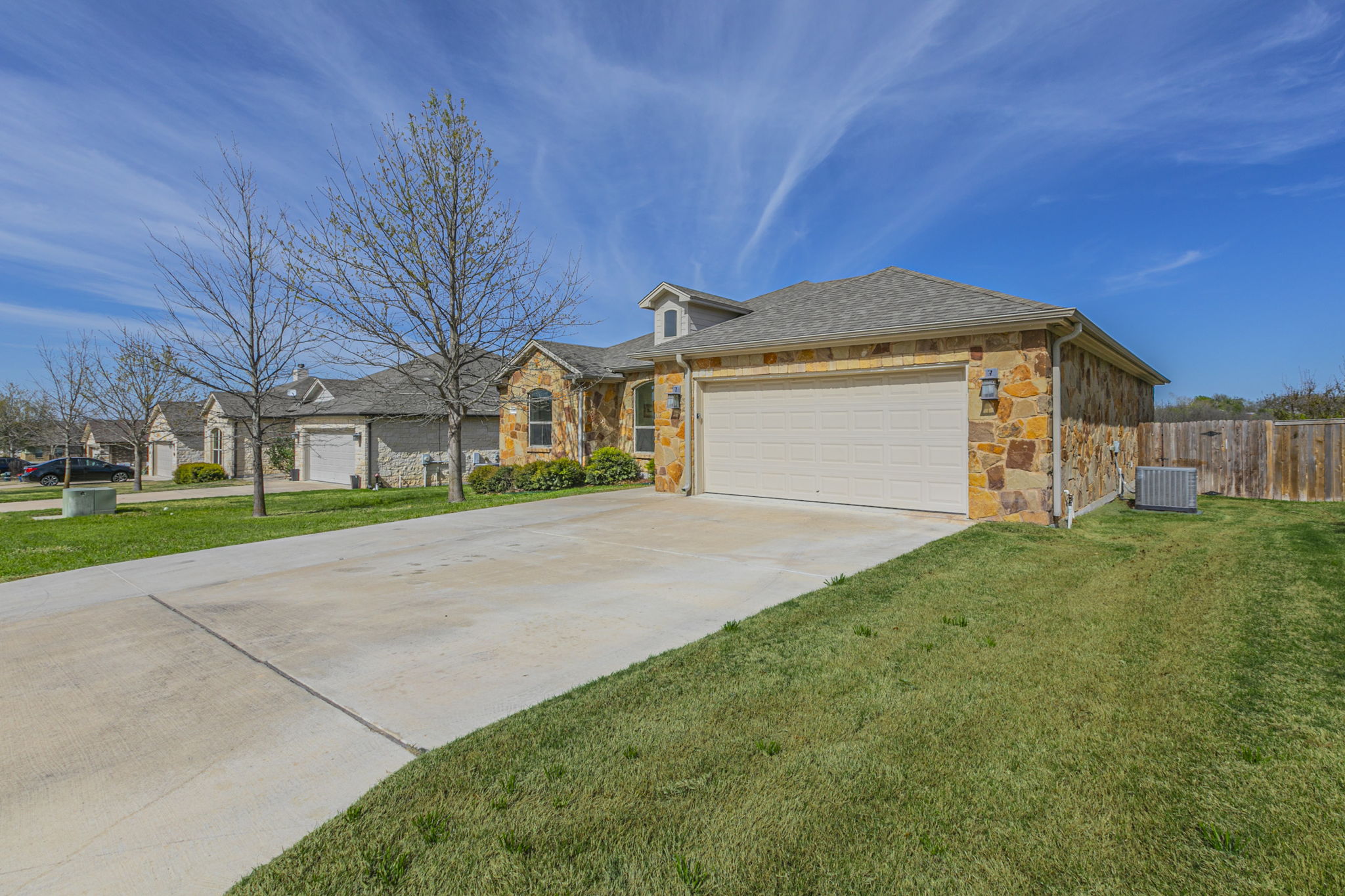 300 Magan Lane Jarrell, TX 76537 - Photo 24 of 33 Ranch-style house with stone siding, an attached garage, concrete driveway, and roof with shingles