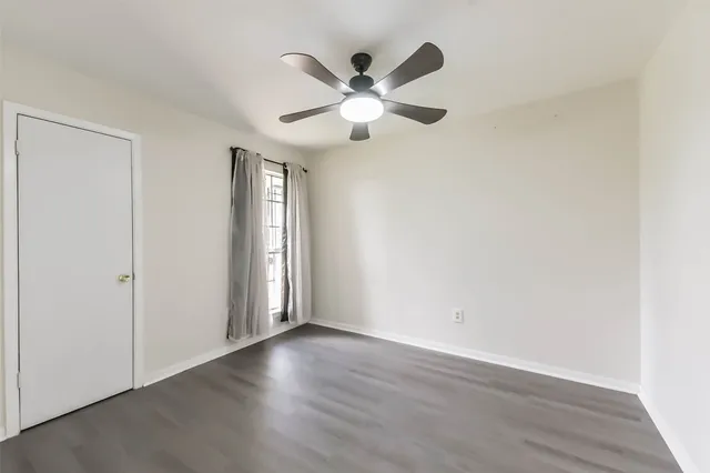 an empty room with wooden floor ceiling fan and windows