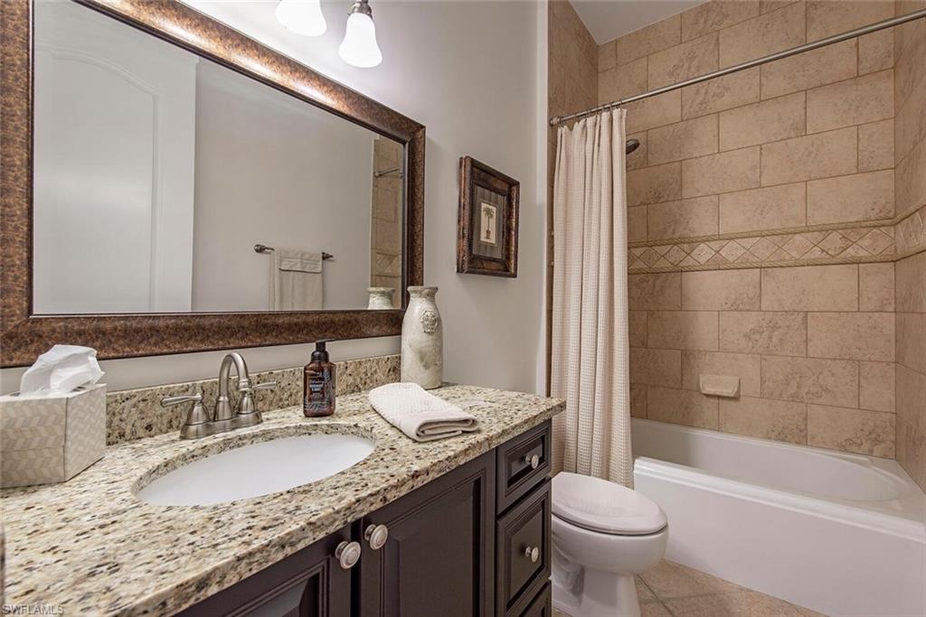 1012 7th Street South, Unit B2 Naples, FL 34102 - Photo 12 of 17 a bathroom with a granite countertop sink a toilet a mirror a bathtub and shower