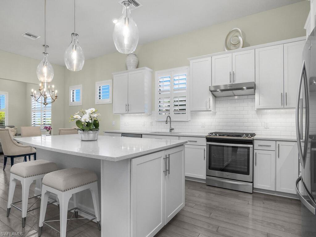 a kitchen with stainless steel appliances granite countertop a sink a stove a refrigerator and island with wooden floor