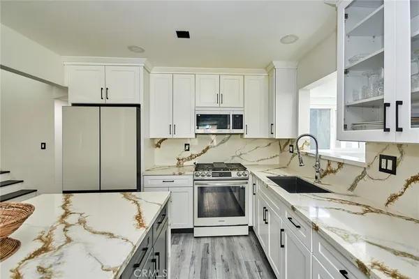 a kitchen with stainless steel appliances a stove a sink a refrigerator white cabinets and wooden floor