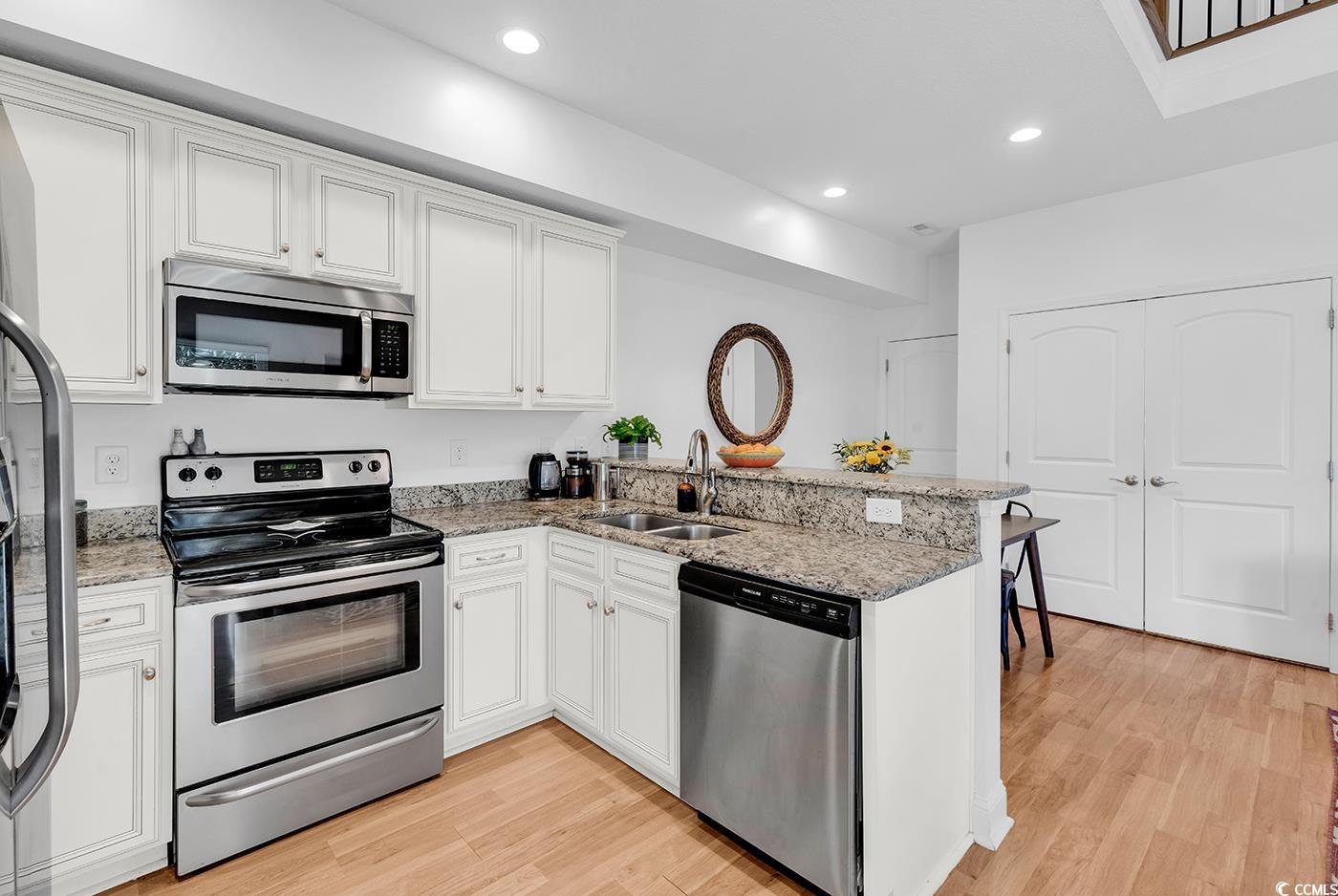 327-a&b Sparrow Drive Surfside Beach, SC 29575 - Photo 5 of 33 Kitchen featuring appliances with stainless steel finishes, a peninsula, white cabinets, light wood finished floors, and light stone counters