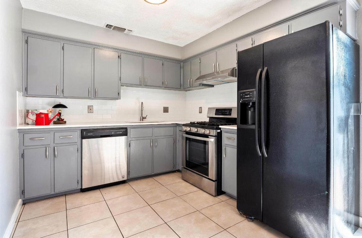 2405 Parker Circle, Unit B Georgetown, TX 78628 - Photo 20 of 23 Kitchen featuring gray cabinetry, stainless steel appliances, light tile patterned floors, under cabinet range hood, and backsplash