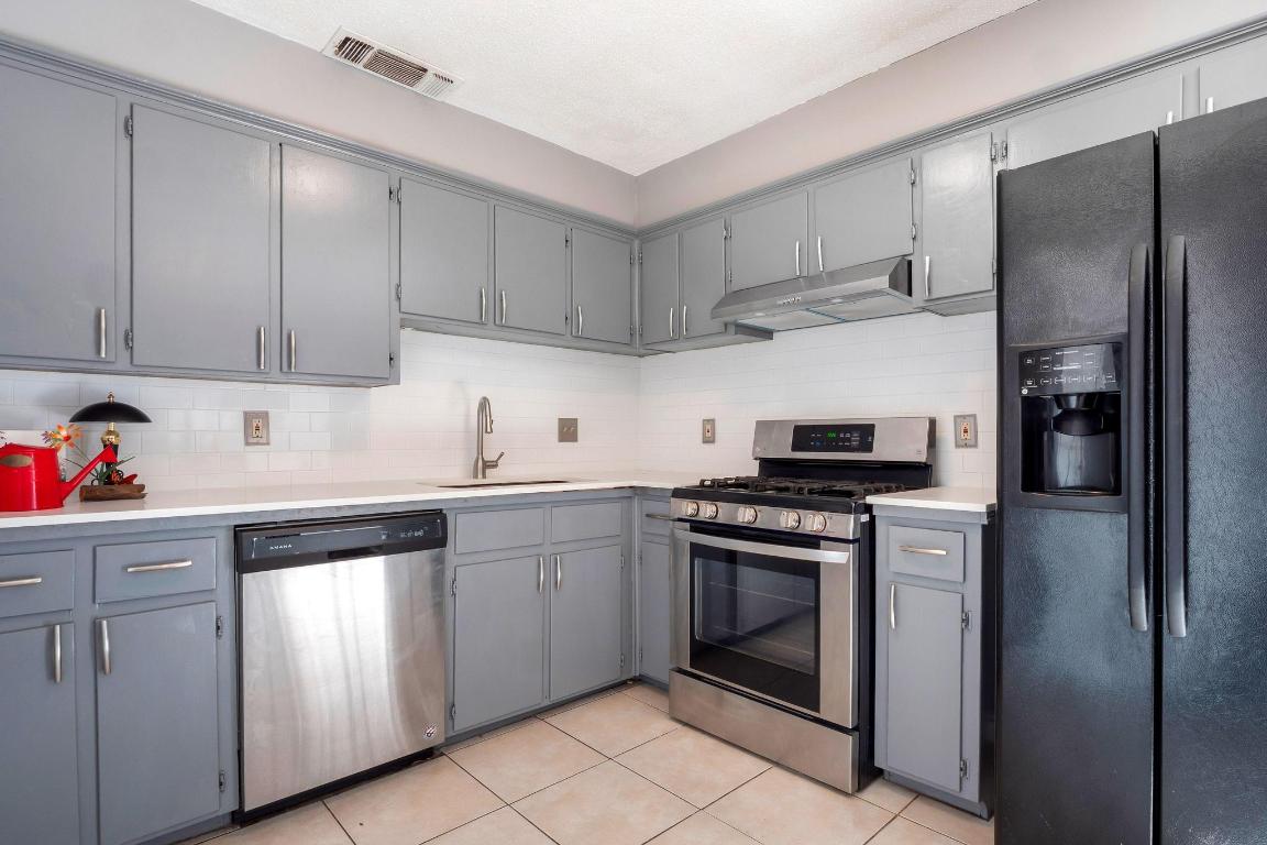 2405 Parker Circle, Unit B Georgetown, TX 78628 - Photo 21 of 23 Kitchen featuring stainless steel appliances, gray cabinetry, under cabinet range hood, backsplash, and light tile patterned floors