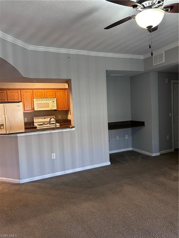 12975 Positano Circle, Unit 307 Naples, FL 34105 - Photo 1 of 6 Kitchen featuring brown cabinetry, fridge, dark countertops, ornamental molding, and dark carpet