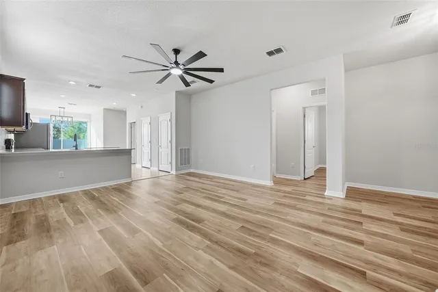 a view of an empty room with wooden floor and a ceiling fan