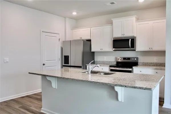 a kitchen with granite countertop a refrigerator a stove a sink and white cabinets with wooden floor