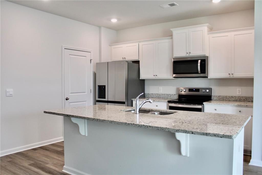 102 Fremont Lane Pooler, GA 31322 - Photo 3 of 10 a kitchen with granite countertop a refrigerator a stove a sink and white cabinets with wooden floor