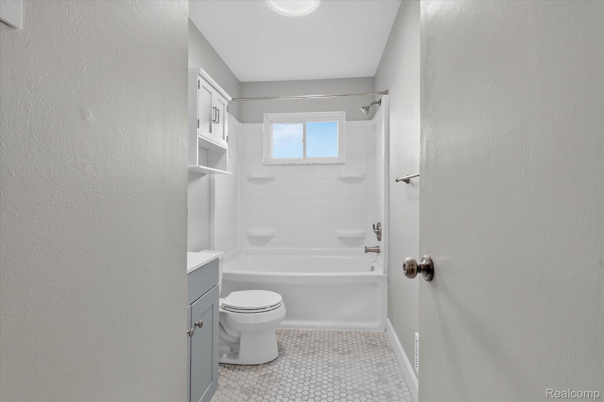 934 Harvard Road Berkley, MI 48072 - Photo 18 of 34 Full bathroom featuring a white bathtub and shower surround, light gray vanity with under-sink storage, a matching wall-mounted cabinet, and hexagonal floor tiling