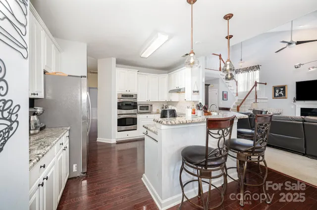 a kitchen with stainless steel appliances kitchen island granite countertop a table chairs refrigerator and microwave