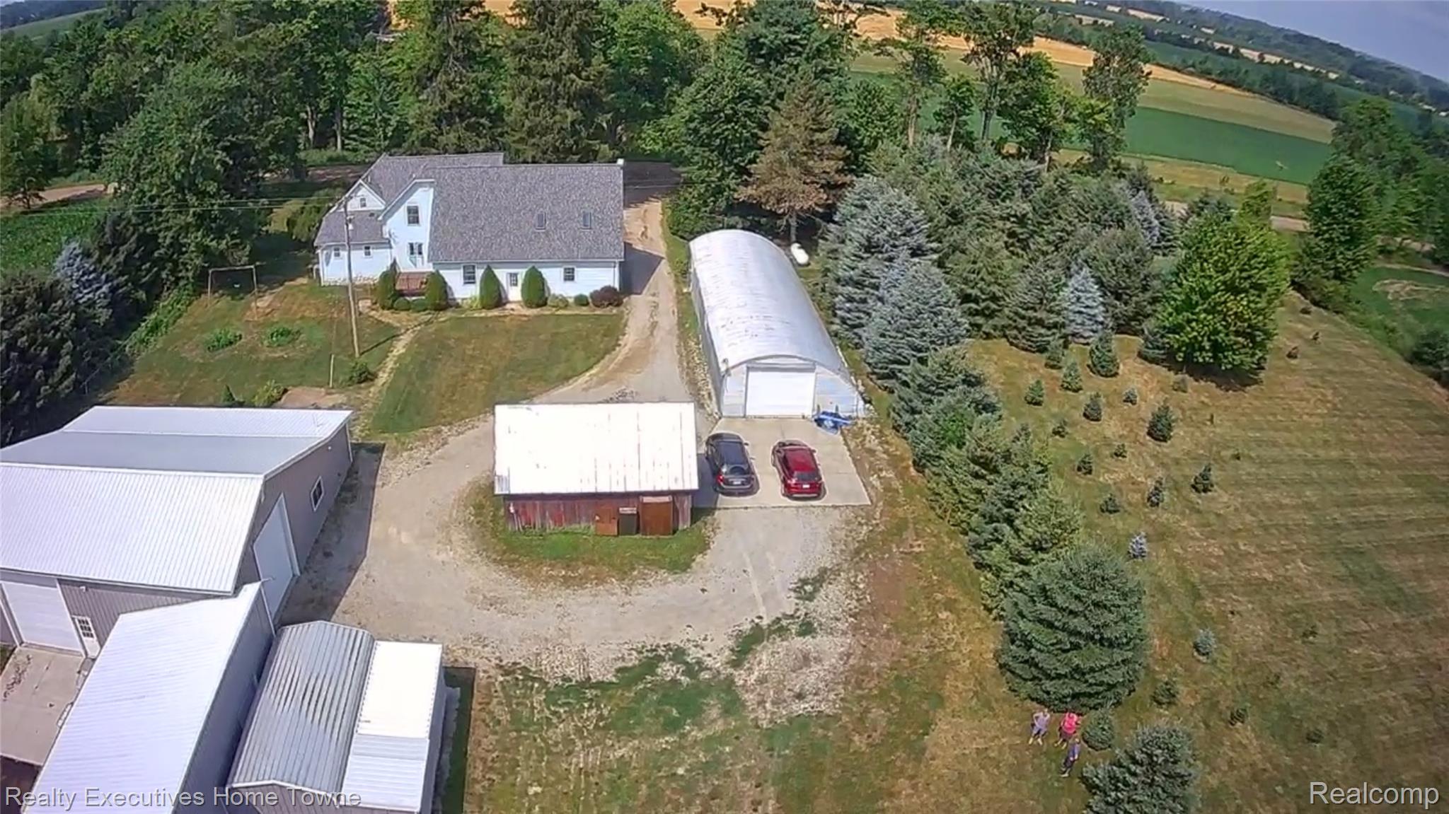 2715 Cash Road Applegate, MI 48401 - Photo 19 of 59 Aerial perspective showcasing a single-family home with a light-colored exterior and dark shingle roof, accompanied by multiple outbuildings including a large metal structure, a smaller red-sided barn, and a hoop house