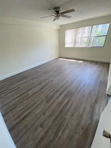 an empty room with wooden floor fan and windows