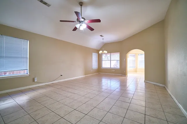 a view of an empty room with window and chandelier fan