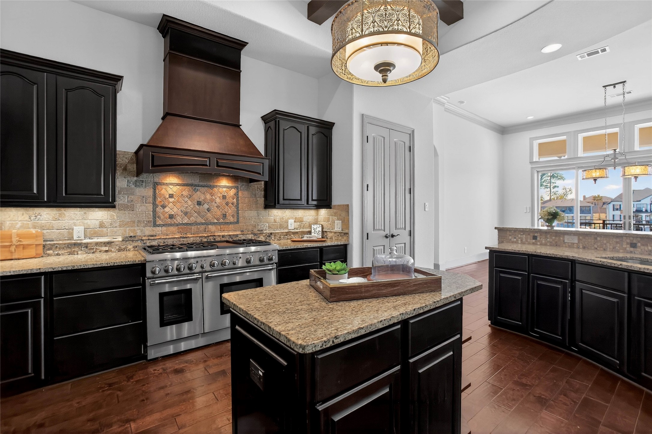 12349 Tramonto Conroe, TX 77304 - Photo 16 of 50 The kitchen includes an island with a tray centerpiece, a stylish tile backsplash, and a decorative light fixture. The space is bright with natural light from adjacent windows.