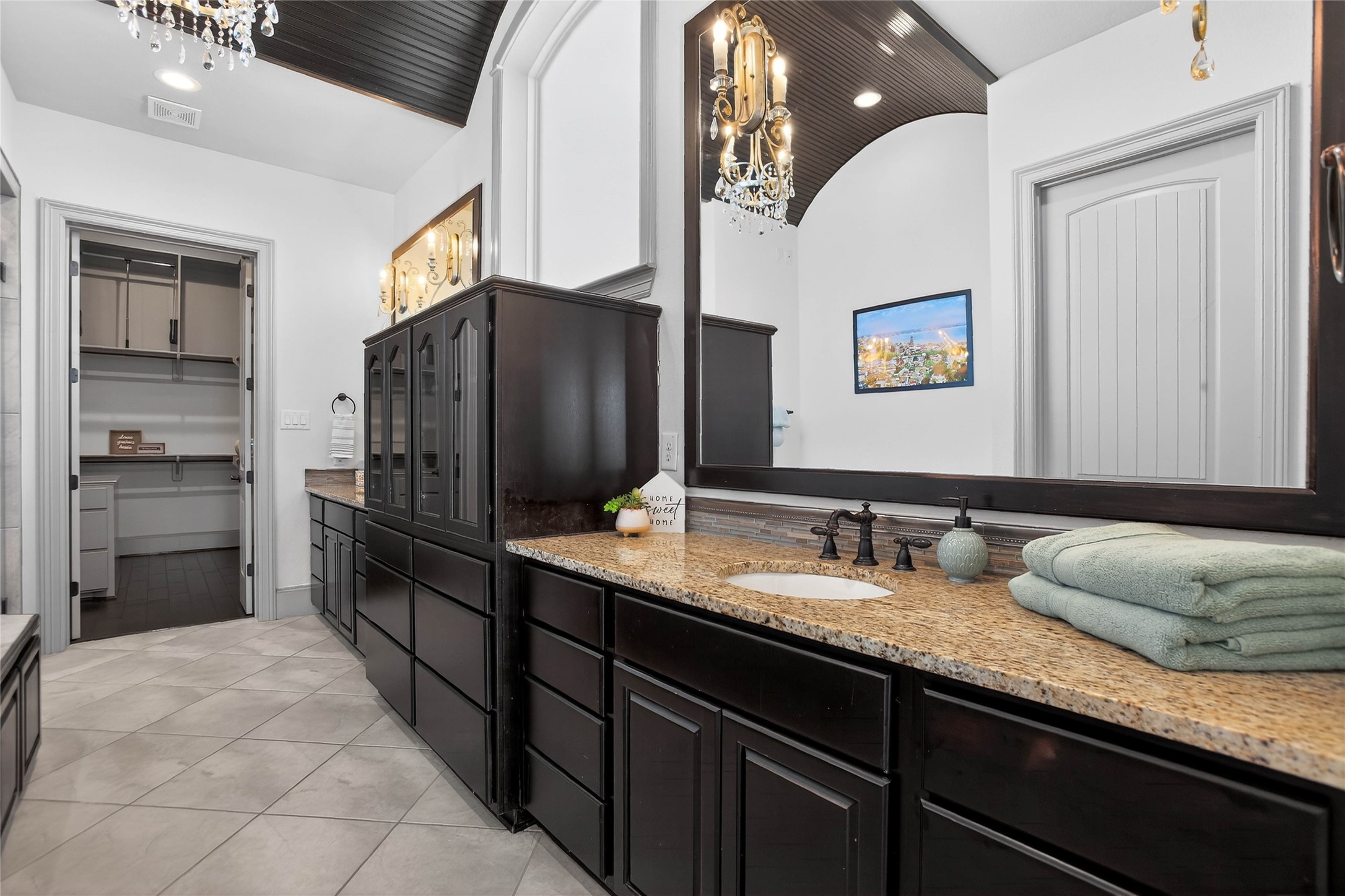 12349 Tramonto Conroe, TX 77304 - Photo 21 of 50 This spacious bathroom features elegant chandeliers, dark wood cabinetry, and granite countertops. It includes dual sinks, two large mirrors, and a walk-in closet, offering both style and functionality.