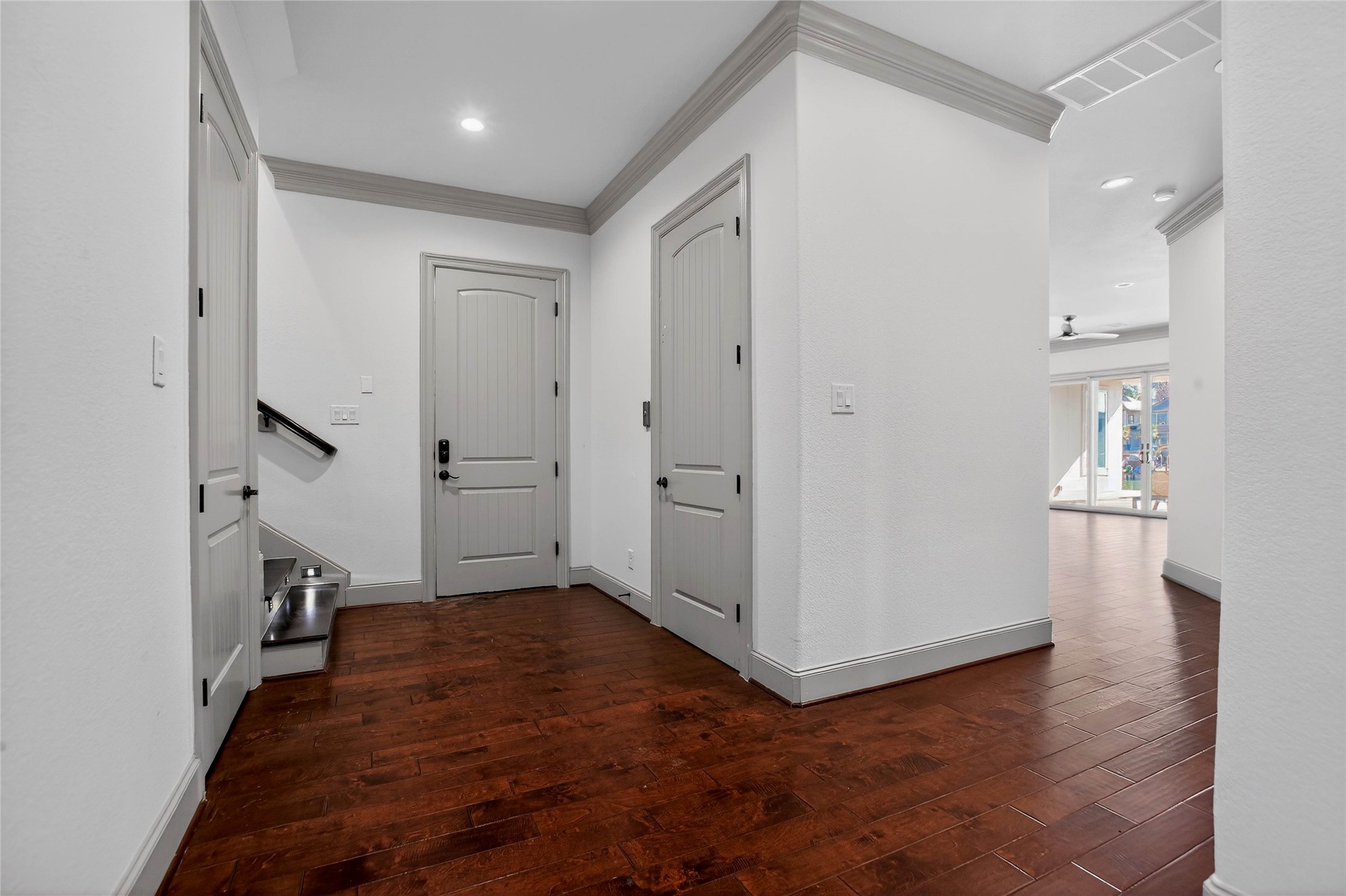 12349 Tramonto Conroe, TX 77304 - Photo 35 of 50 This photo showcases a bright, open hallway with rich hardwood flooring and neutral walls on the first floor. It features elegant crown molding, a staircase to the left, and leads to a spacious living area with large windows offering plenty of natural light.