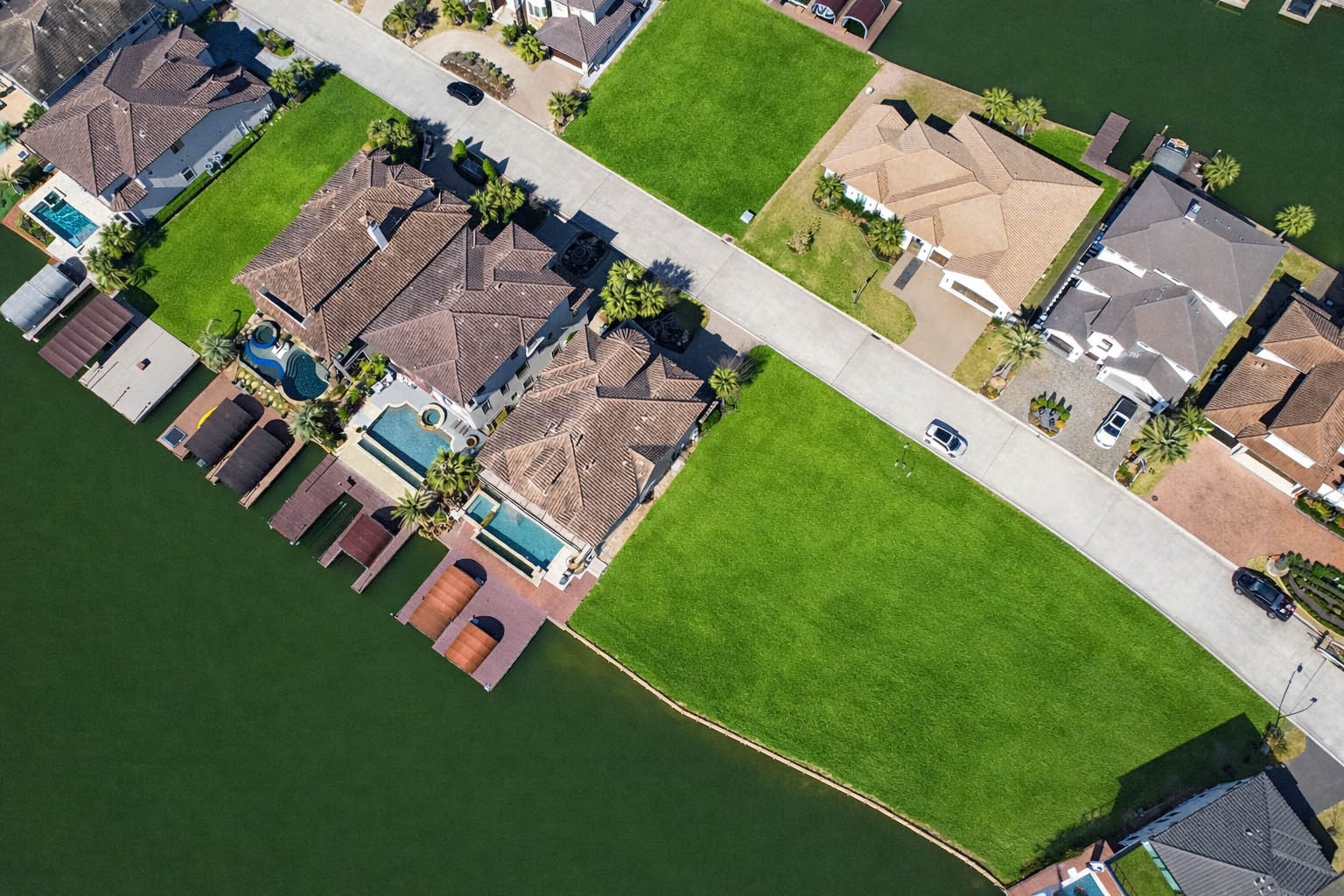 12349 Tramonto Conroe, TX 77304 - Photo 45 of 50 This aerial photo showcases a picturesque waterfront neighborhood with luxury homes featuring pools and private docks. The houses are set along a canal, with lush green lawns and a spacious street, offering a serene and upscale residential environment.