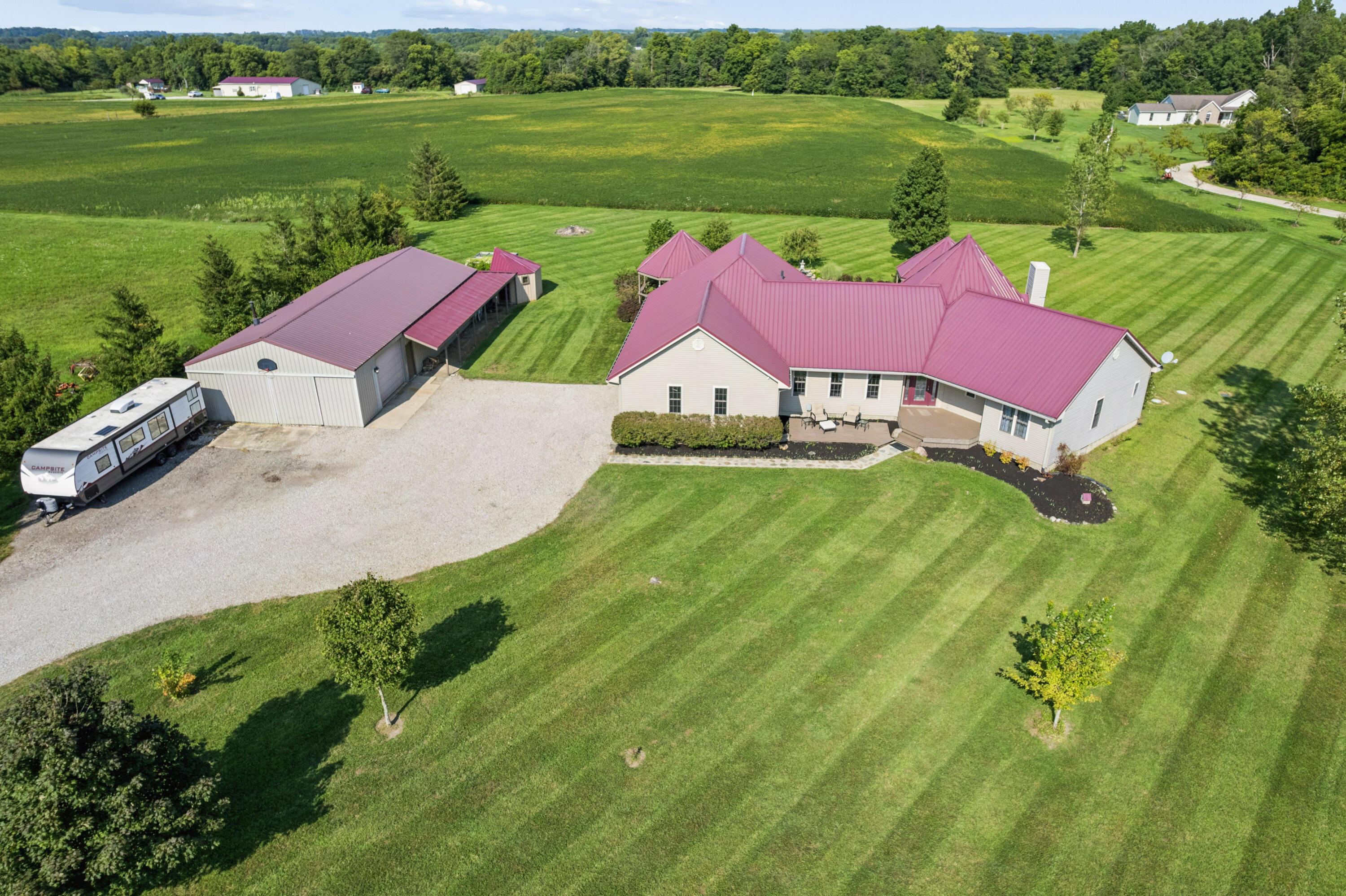 18964 London Road Circleville, OH 43113 - Photo 2 of 57 Expansive green lawn surrounds a single-story residence with a burgundy metal roof and an accompanying large detached pole barn