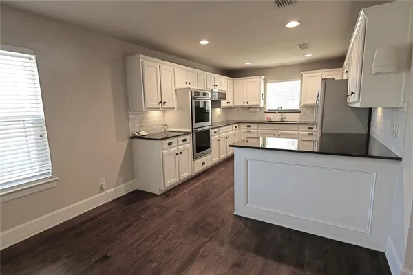 a kitchen with stainless steel appliances granite countertop a refrigerator a stove a sink and white cabinets with wooden floor
