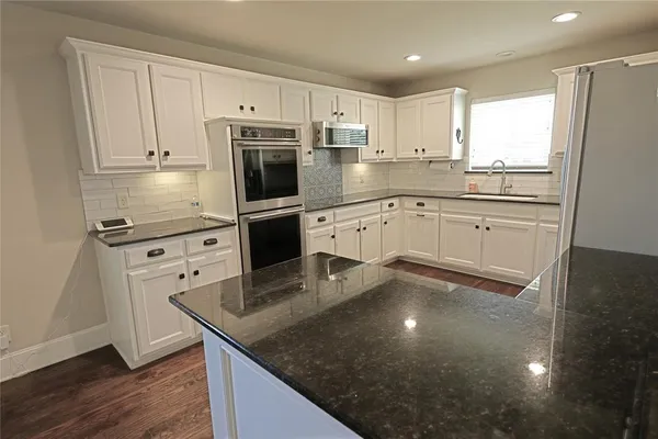 a kitchen with stainless steel appliances granite countertop a sink a stove a refrigerator and white cabinets with wooden floor