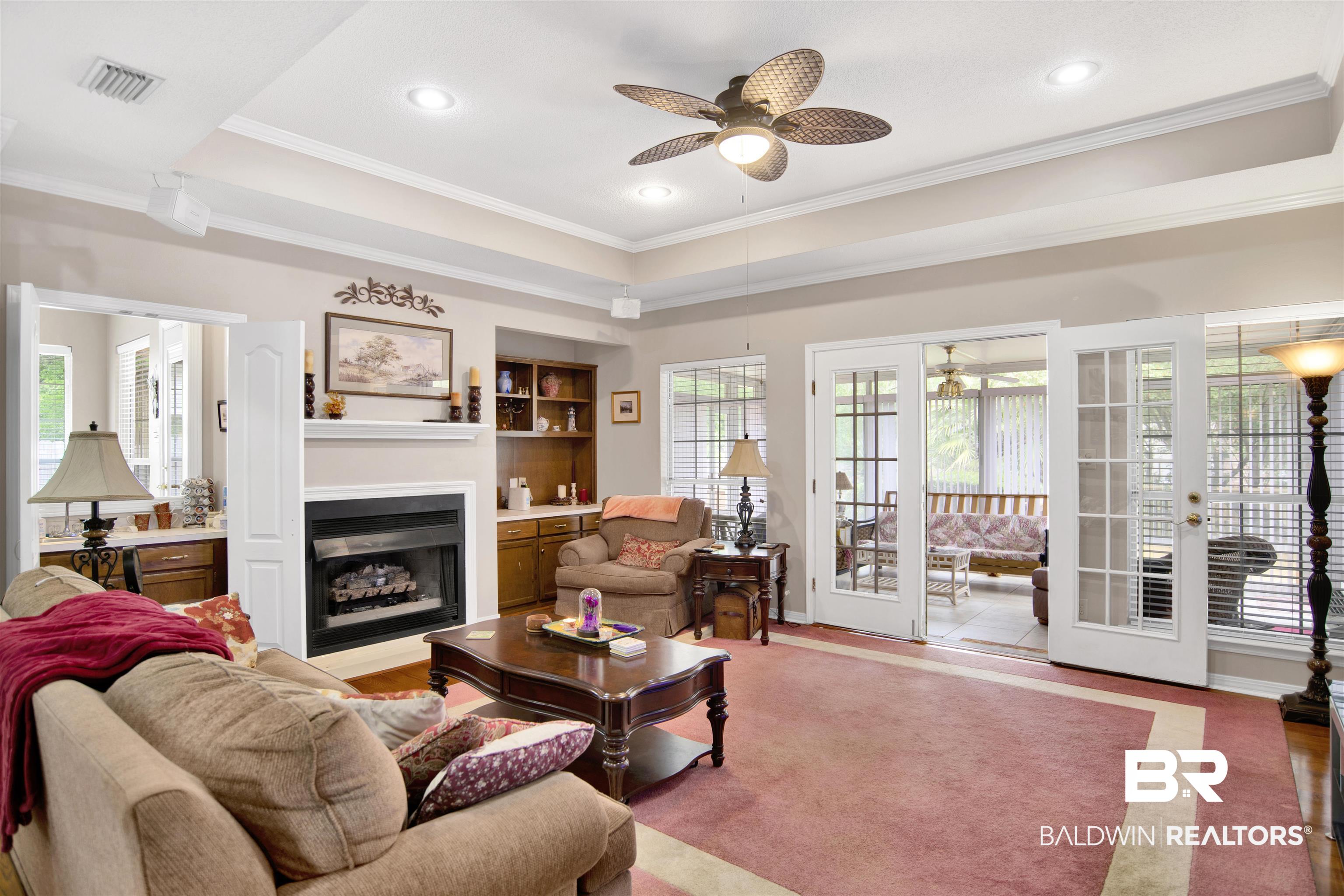 107 Virginia Circle Daphne, AL 36526 - Photo 9 of 47 Living area featuring a fireplace with a mantel, built-in shelving, tray ceiling with recessed lighting and a ceiling fan, and French doors opening to an enclosed porch