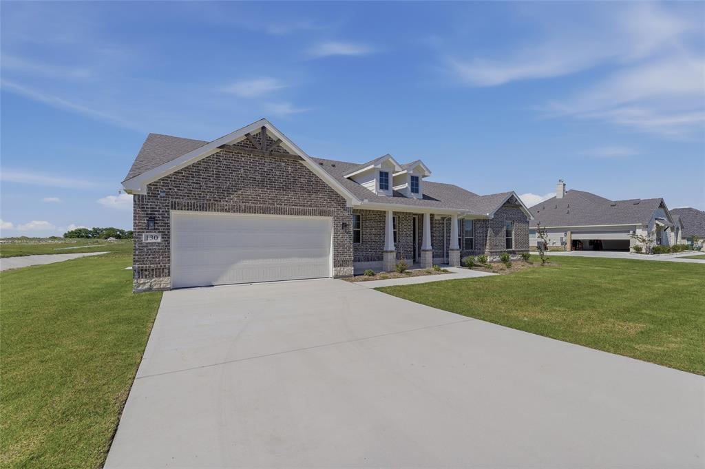 130 Fossil Canyon Drive Rhome, TX 76078 - Photo 2 of 25 Brick exterior featuring a two-car garage, concrete driveway, and front porch with columns