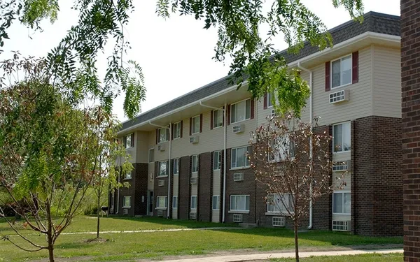 a view of a white house with a large windows and a yard with plants and large trees