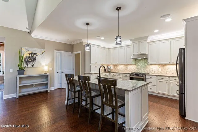 a kitchen with stainless steel appliances granite countertop a stove a refrigerator a kitchen island and chairs with wooden floor