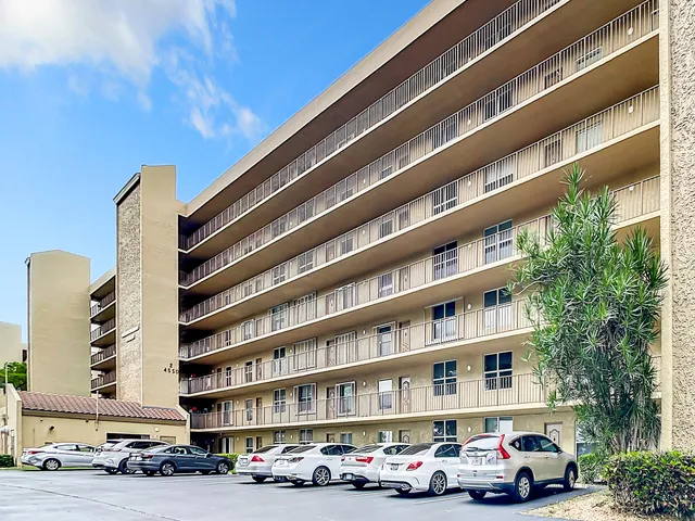 a front view of a building with lot of cars and trees