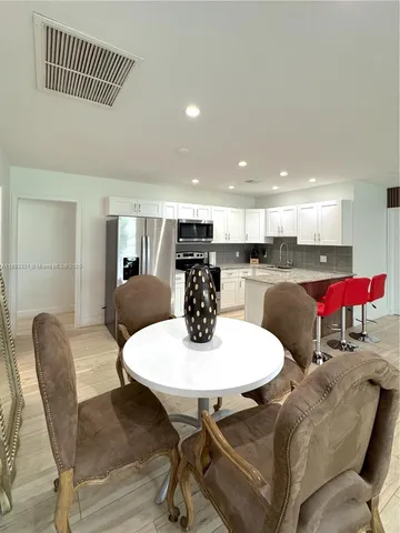 a kitchen with stainless steel appliances kitchen island granite countertop a dining table chairs and a refrigerator