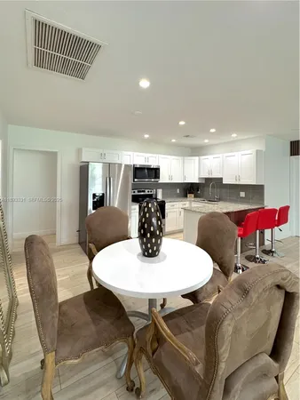 a kitchen with stainless steel appliances kitchen island granite countertop a dining table chairs and a refrigerator