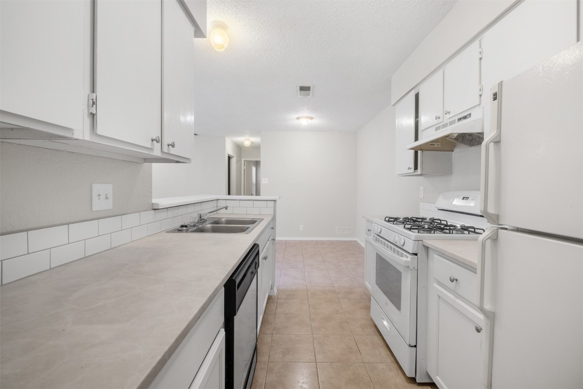 12901 Chromite Street, Unit B Austin, TX 78727 - Photo 14 of 21 Kitchen with white appliances, white cabinetry, light countertops, under cabinet range hood, and a textured ceiling