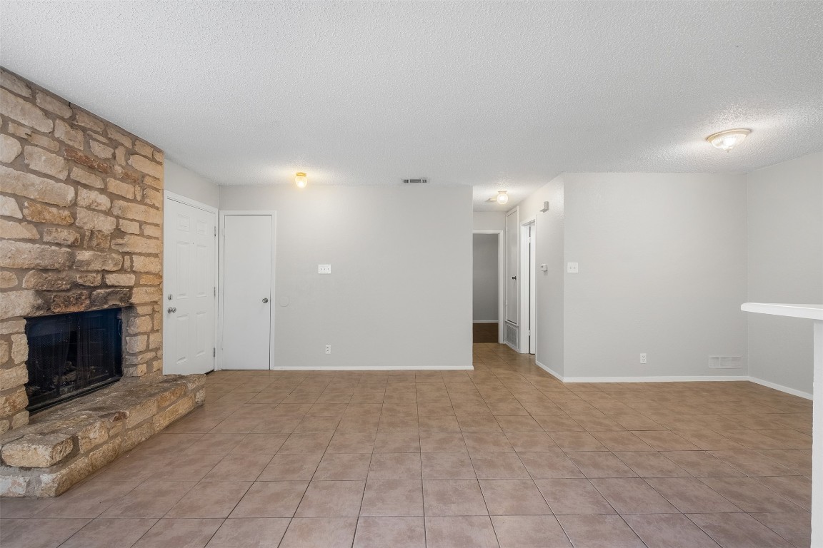 12901 Chromite Street, Unit B Austin, TX 78727 - Photo 4 of 21 Unfurnished living room with a textured ceiling, a stone fireplace, and light tile patterned flooring