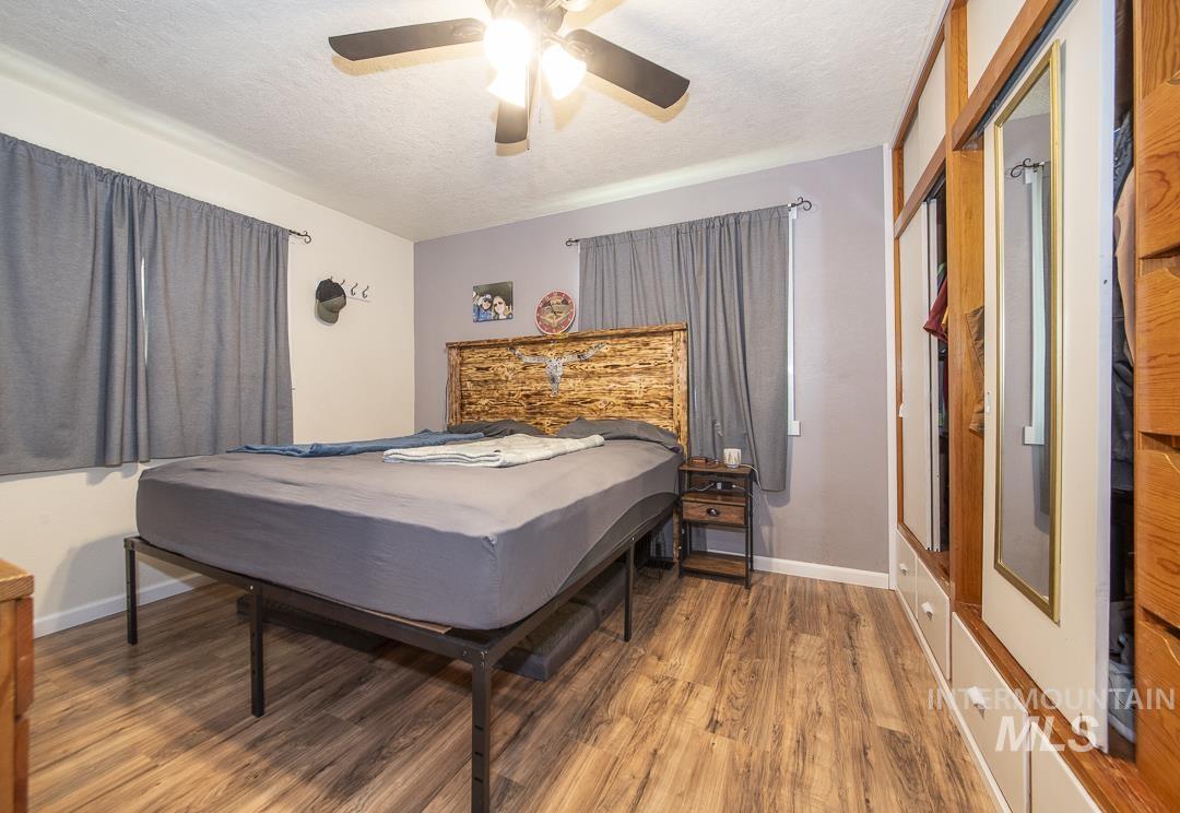 486 West Main Street South Vale, OR 97918 - Photo 22 of 37 Bedroom featuring wood-finish flooring, two windows with curtain rods, a ceiling fan with integrated lighting, and a built-in closet system with mirrored doors and lower drawers