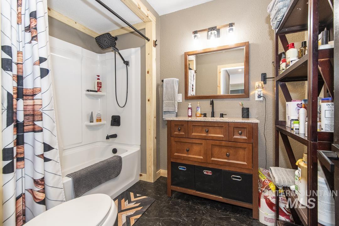 486 West Main Street South Vale, OR 97918 - Photo 24 of 37 Full bathroom featuring a white tub/shower combination with a matte black showerhead, a wood-finish vanity with a stone-finish countertop, and dark wood-finish open shelving