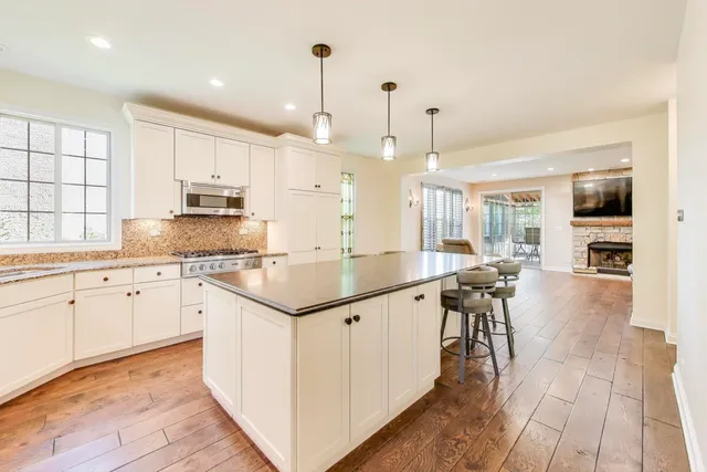 a kitchen with stainless steel appliances granite countertop a stove top oven a sink a dining table and chairs with wooden floor