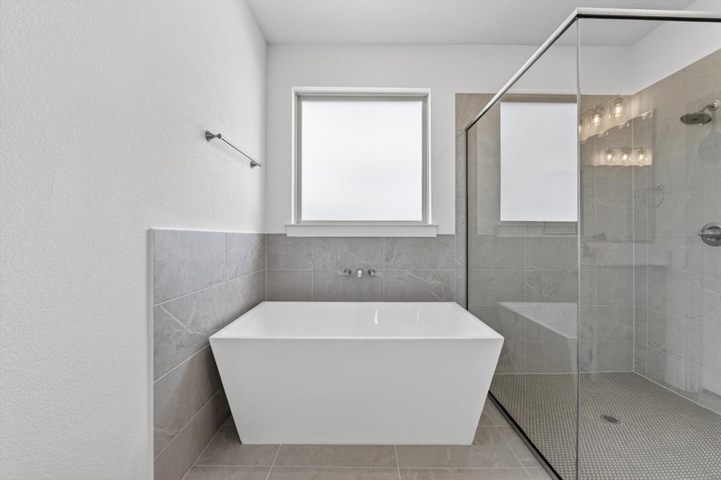416 McAlpine Drive Springtown, TX 76082 - Photo 27 of 40 Freestanding soaking tub with wall-mounted faucet, complemented by a glass-enclosed walk-in shower featuring a built-in bench