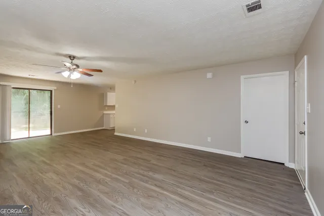 a view of an empty room with wooden floor and a ceiling fan