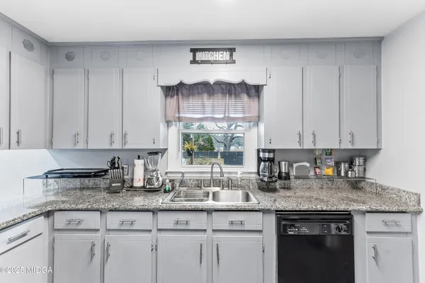 a kitchen with granite countertop a sink white cabinets and a wooden floor