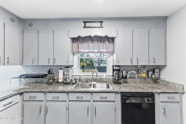 a kitchen with granite countertop a sink white cabinets and a wooden floor
