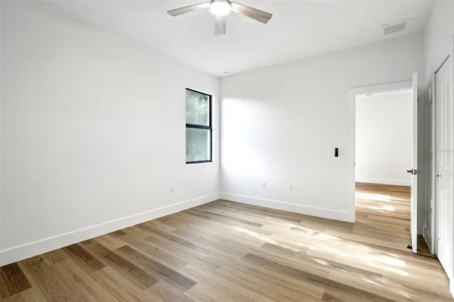 an empty room with wooden floor chandelier fan and windows