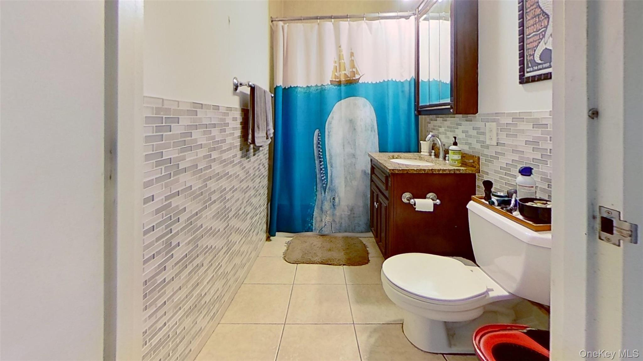 116-12 Ocean Promenade, Unit 210 Queens, NY 11694 - Photo 19 of 28 Full bathroom with light tile patterned floors, vanity, a shower with shower curtain, tile walls, and wainscoting