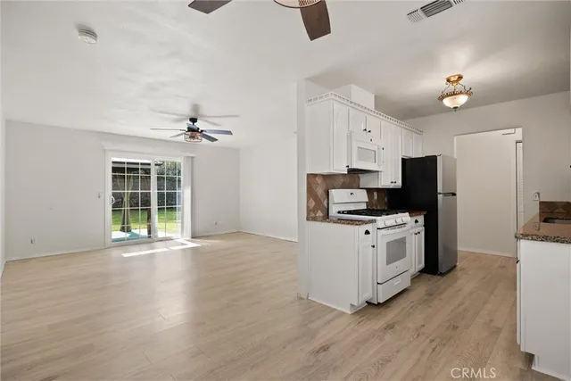 a kitchen with stainless steel appliances granite countertop a stove top oven a sink a refrigerator and white cabinets with wooden floor