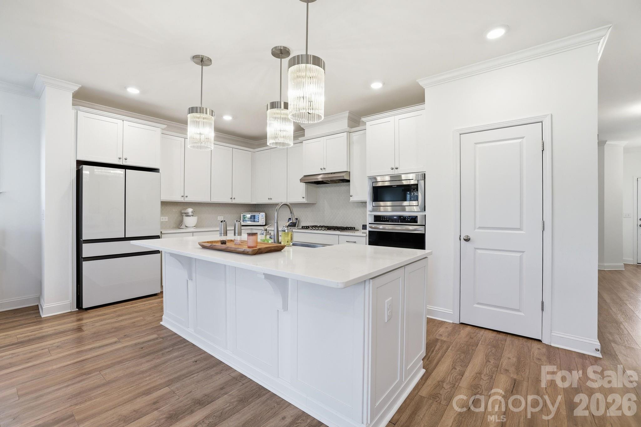 6038 Holland Street Fort Mill, SC 29707 - Photo 10 of 48 a kitchen with kitchen island a sink a stove a refrigerator and white cabinets with wooden floor