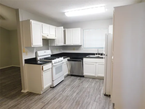 a white kitchen with wooden floors and white appliances