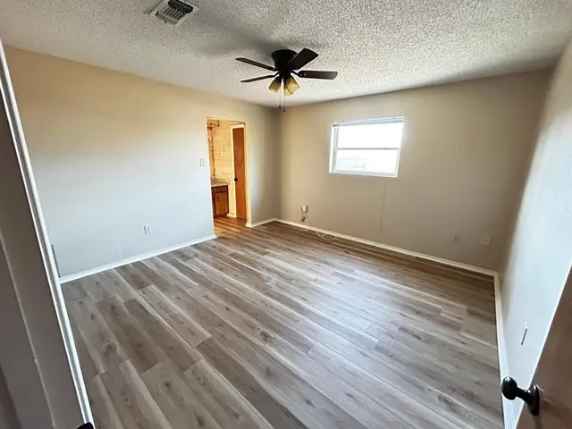an empty room with wooden floor ceiling fan and windows