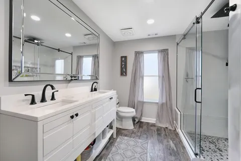a bathroom with a double vanity sink toilet mirror and windows