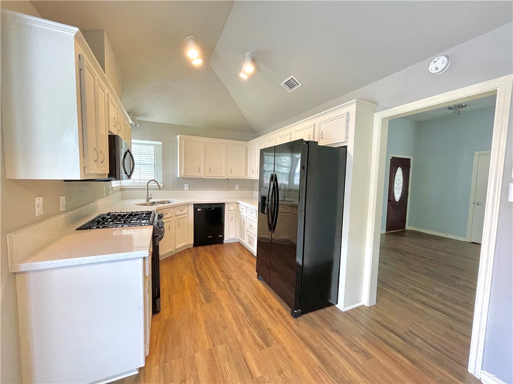 4508 Kensington Road Bryan, TX 77802 - Photo 6 of 25 Kitchen with sink, white cabinetry, black appliances, light hardwood / wood-style floors, and vaulted ceiling